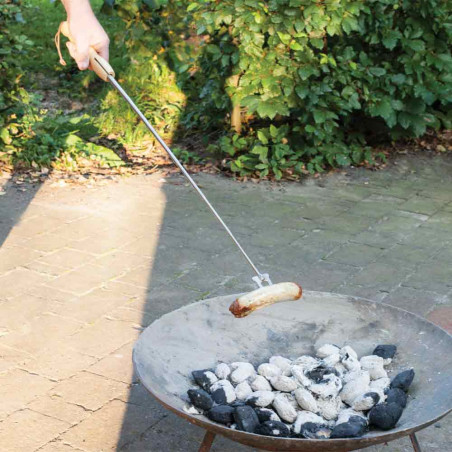 Homme faisant griller une saucisse sur un brasero avec la fourchette télescopique Esschert