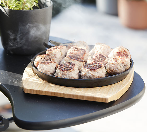 Boulettes de viande dans la poêle en fonte Barbecook et dessous de plat en bambou posé sur une tabllette de barbecue kamado Kamal