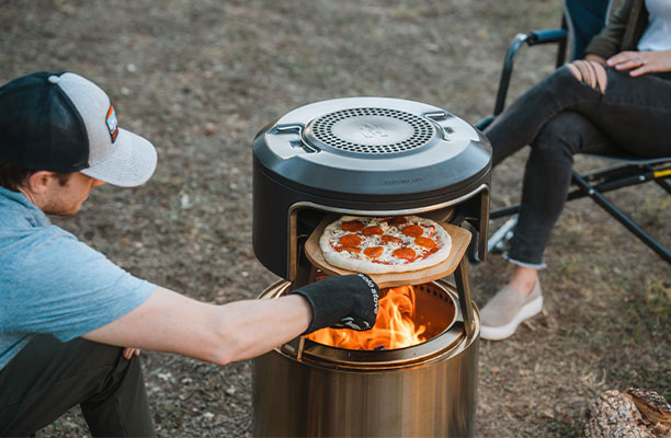 Homme qui enfourne une pizza dans le four à pizza Pi Fire Solo Stove dans le brasero Bonfire