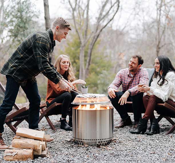 Personne posant le pare-étincelles en inox sur le brasero Bonfire Solo Stove, installé sur une terrasse en cailloux