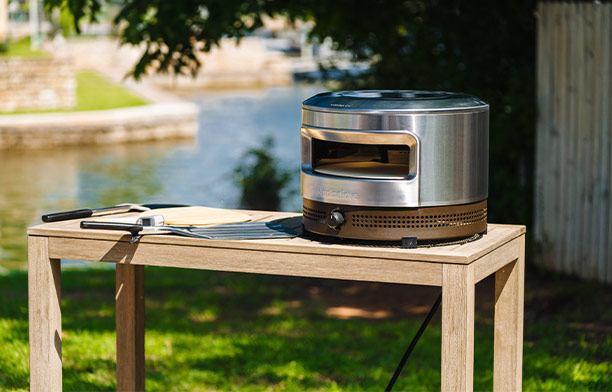 Four à pizza gaz Pi Prime Solo Stove posé sur une table de salon de jardin en bois