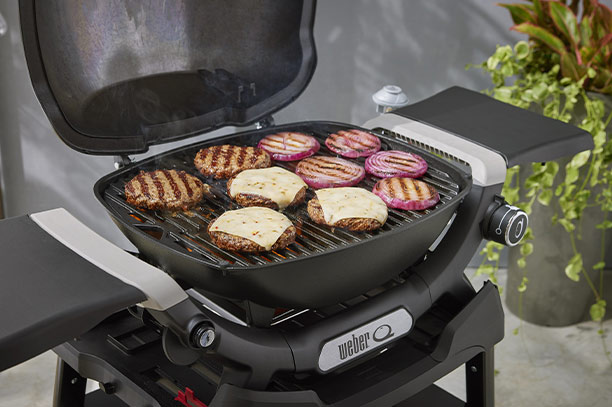 Cuisson d'aliments sur les grilles en fonte émaillée du barbecue gaz Q 1200 N noir sur stand Weber